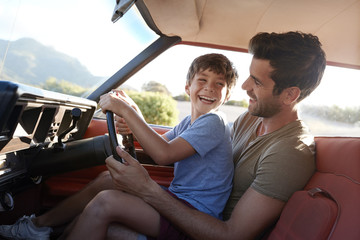 Father Teaching Young Son To Drive Car On Road Trip