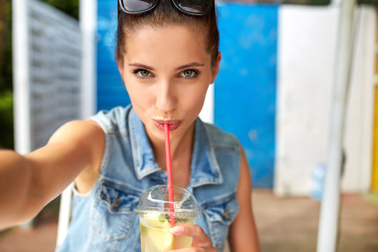 Lovely young smiling woman drinking lemonade and make a selfie.