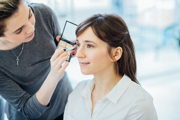 Backstage scene: Professional Make-up artist doing make up for young beautiful brunette woman.