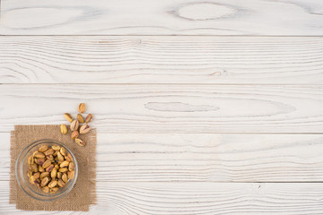 Pistachio nuts in a glass bowl on an old white wooden table.