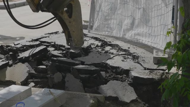 Excavator with hydrohammer drill breaking asphalt of the street