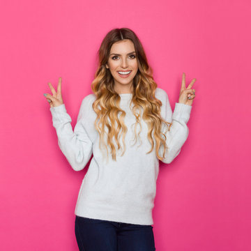 Young Smiling Woman In Pastel Sweater Is Showing Peace Hand Sign