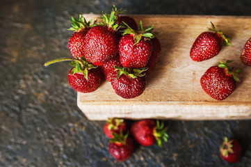 A juicy ripe strawberry lies on a wooden tray on a dark textural background. Strawberry and a centimeter. Healthy eating. Fruits, detox
