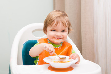 Happy baby sitting in high chair  eats itself with a spoon