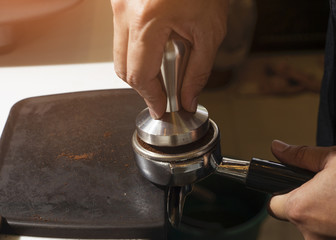 Close-up Barista pressing ground coffee into portafilter by tamper to making coffee