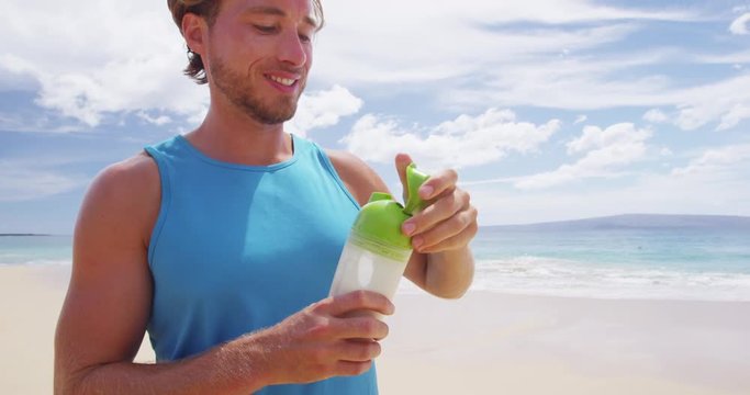 Man drinking protein drink after shaking sports bottle with protein powder mix outside on beach.