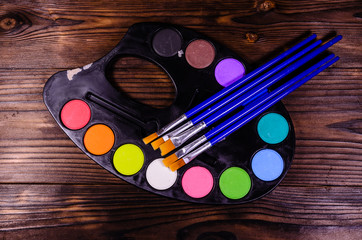 Watercolor paints and paintbrushes on wooden table. Top view