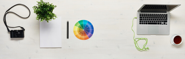Aerial wide view of designer desk with computer, colour wheel, paper, pencil, camera, headphones,...