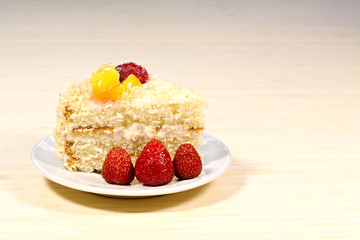 Sliced tasty cake with straberry and peach on wooden background