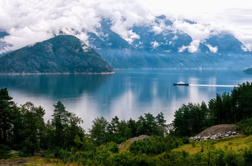 White ship on the background of mountains and forest covered with clouds .