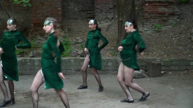 Young women in green costumes dancing near the tree in the yard