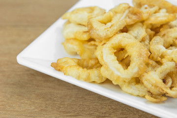crispy deep fried squid ring in white plate on wooden surface, close up