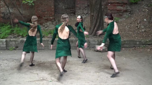 Group of young women in costumes dancing near the tree in the yard