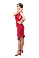 Side view of young woman in red dress touching hair looking at camera.  Full body length portrait isolated on white studio background. 