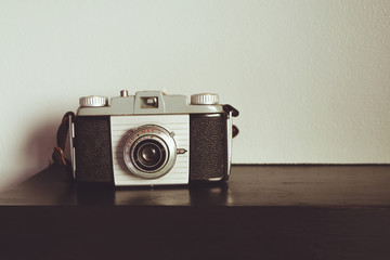 Retro old outdated rangefinder film camera from 50s on table front wall background. Vintage style filtered photo