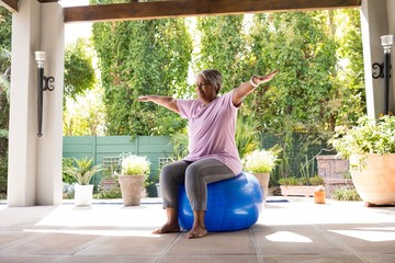 Senior woman with arms outstretched sitting on exercise ball - Powered by Adobe