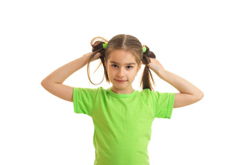 a wonderful little girl in a bright t-shirt keeps hands their ponytails and looks into a camera