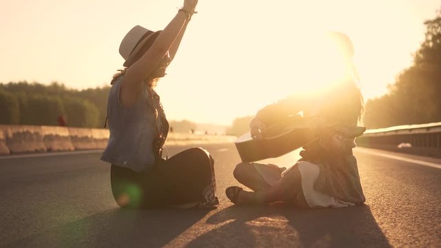 girls hippie sing songs and you play the guitar. two hipsters sitting on the roadway at sunset