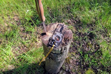 A tourist compass lies in the forest on a stump. Next to him a knife is stuck in the stump.