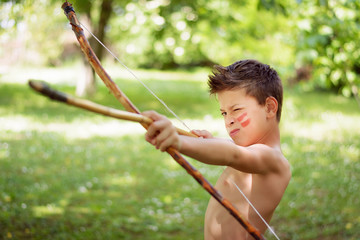 Adorable young boy playing native Indian with toy bow and arrow is aiming and about to shoot