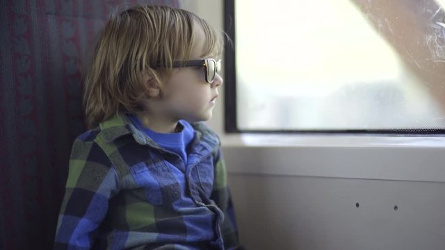 Little Boy Enjoys Train Ride, Looks Out Window As The Train Goes Over A Bridge 