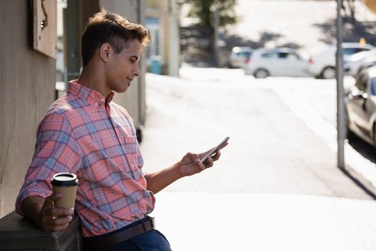 Young Man Using Mobile Phone While Leaning On Wall