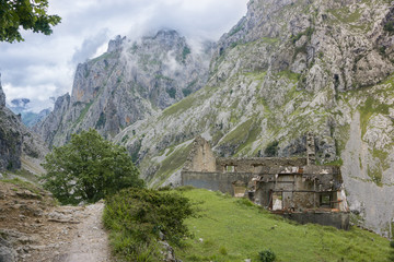 Fototapeta na wymiar Beautiful landscape of the mountains in Picos de Europa in Spain; hiking trail in foggy and cloudy summer day: ruins of abandoned stone house
