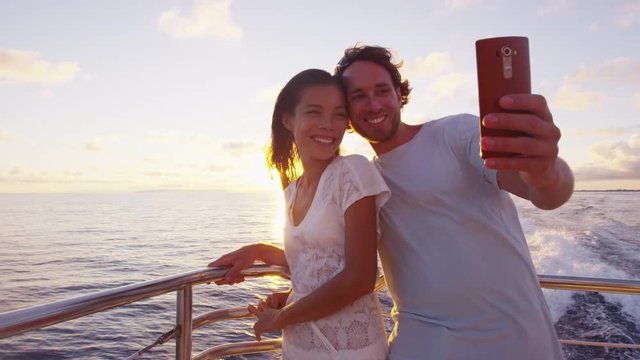 Smart phone selfie - Romantic couple taking phone selfie by sunset over the ocean on small cruise ship sailing on open sea on vacation.
