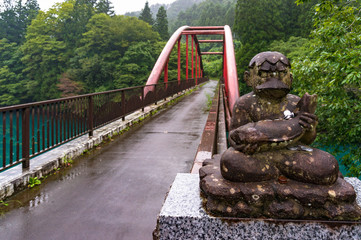 Red arch bridge and old statue with fish and coin donations