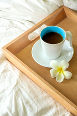 coffee cup in wood tray on the bed background in the morning time.