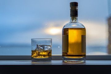 Amber colored alcohol drink with bottle on rainy window sill