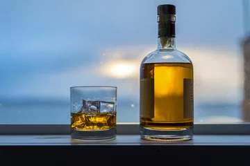 Plexiglas foto achterwand Amber colored alcohol drink with bottle on rainy window sill © Richard
