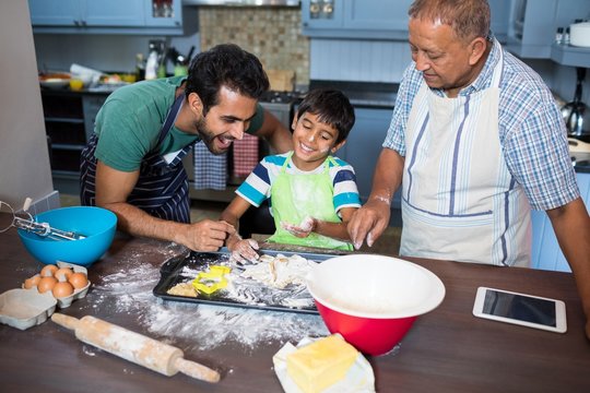 Boy preparing food while standing with father and grandfather