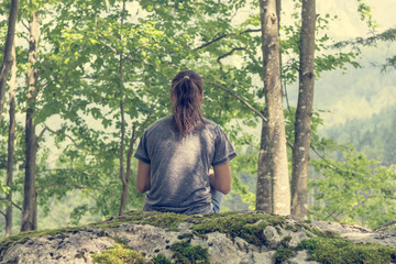 Young woman meditating on forest rock.
