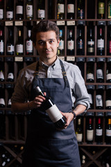 Portrait of a sommelier standing in a wine cellar holding a glass of wine and showing thumb up, during a degustation - obrazy, fototapety, plakaty
