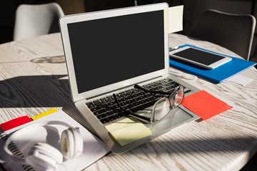 Laptop computer with eyeglasses on wooden table