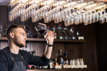 Skilled sommelier pouring wine. Man in black suit and white shirt looks concentrated: he's evaluating quality of wine being pouring. Process of tasting wine captured in photo.