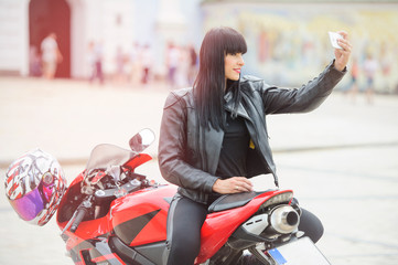 Freedom and style. Colorful portrait of a young woman with a red motorcycle. Girl biker holding phone in hand
