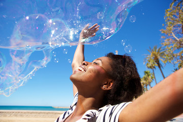 Young african woman playing with soap bubbles outdoors at beach