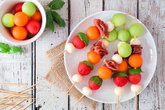Fototapeta Plate of delicious summer fruit skewers with melon, cheese and prosciutto on a rustic white wood background