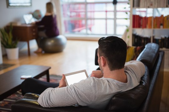 Man using digital tablet while relaxing on sofa in living room