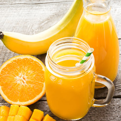 Naklejka na ściany i meble Smoothie with tropical fruits: mango, banana, orange in a glass mason jar on the old wooden background.