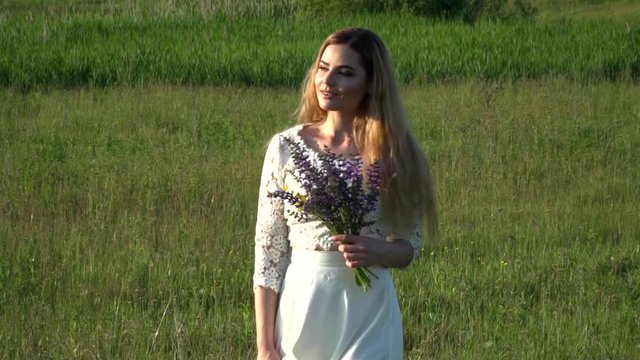 Beautiful young woman gathering flowers on the meadow slow motion