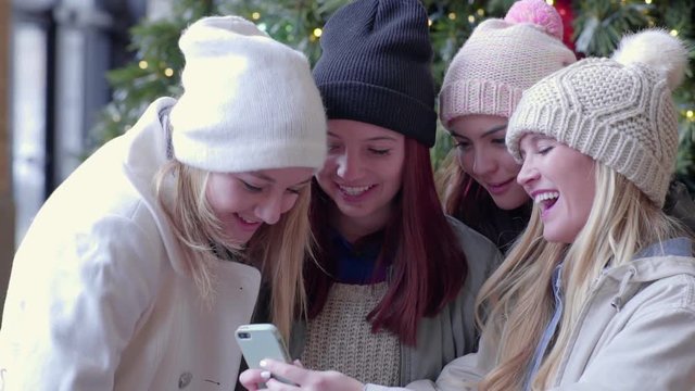 Multi-Ethnic Group Of Teens Take Photos With A Smartphone, They Smile, Laugh, And Pose In Front Of Christmas Tree (Slow Motion) 