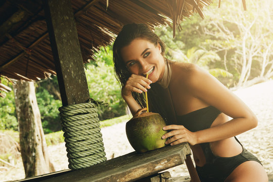Happy woman is enjoying coconut drink in the beach bar