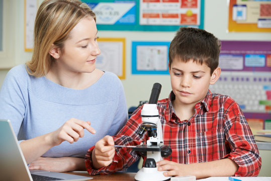 Teacher With Male Student Using Microscope In Science Class