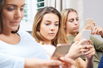 Group Of Teenage Girls Using Mobile Phones At Home