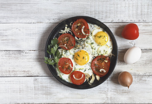 Fried eggs with vegetables and greens (tomatoes, onion, dill) on wooden background. Copy space.