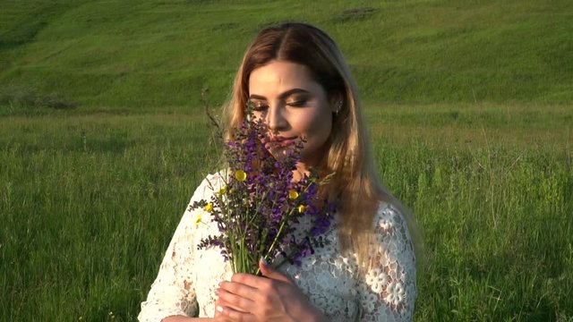 Beautiful woman in white dress with flowers smiling and looking to the camera on the meadow slow motion