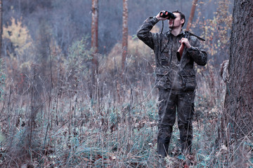 A man in camouflage and with a hunting rifle in a forest on a spring hunt